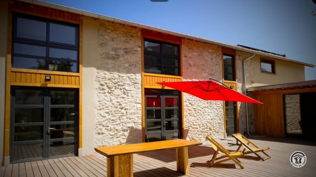 Gîte en pierre avec terrasse en bois et mobilier extérieur.